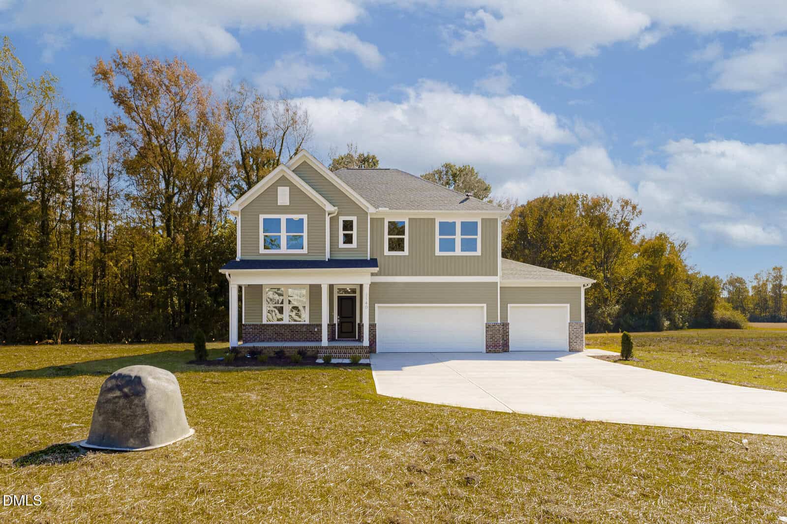 Two-story beige house with white trim and a three-car garage, set on a large grassy lot with a curved concrete driveway at 2140 Old Us 64 in Spring Hope. Trees line the background and the sky is partly cloudy. A gray utility cover sits on the lawn.