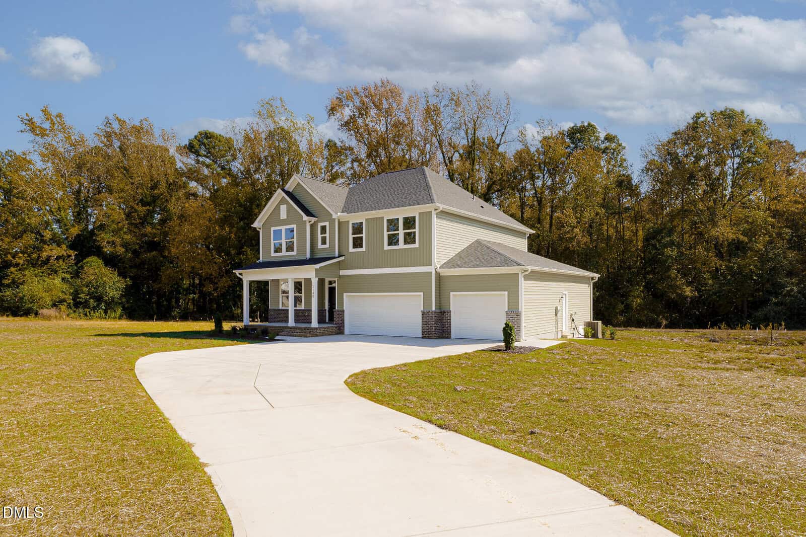 Two-story house with gray siding, white trim, and a three-car garage. The home sits on a large lot with a curved driveway and is surrounded by grass and trees under a partly cloudy sky.