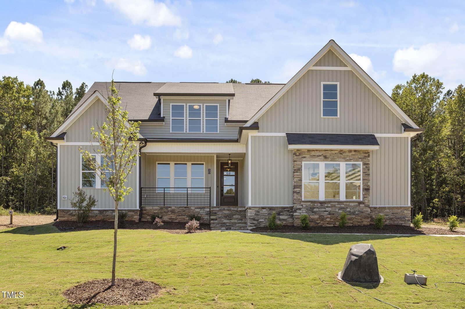 A modern, two-story house at 30 Stream View Way in Zebulon features light siding, stone accents, large windows, and a covered front porch, all set on a freshly landscaped lawn surrounded by trees under a blue sky with scattered clouds.