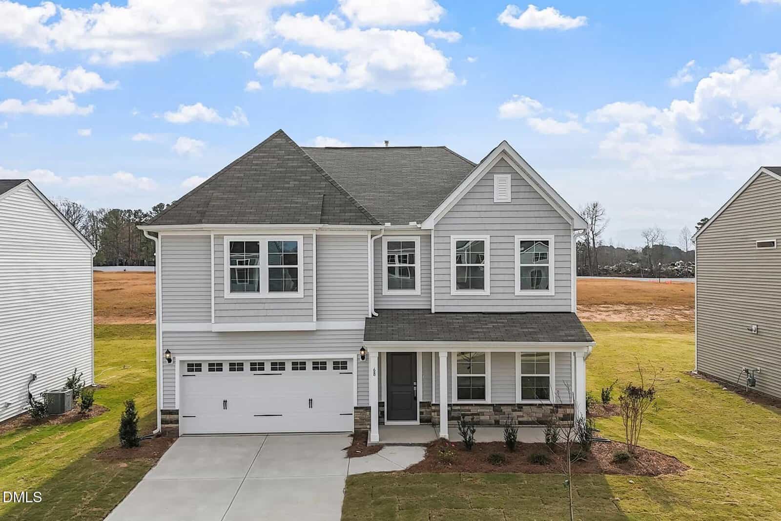 Two-story suburban house with gray siding, a covered front porch, white trim, a double garage, and a neatly landscaped yard located at 68 Plantation Drive in Youngsville. The sky is mostly clear with a few clouds, and neighboring houses are partially visible.