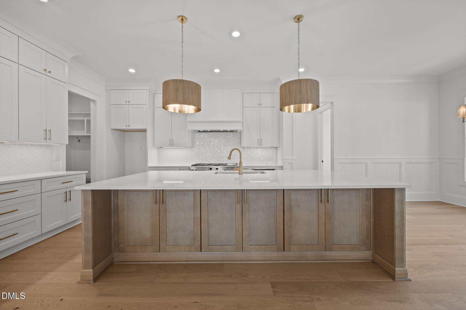 Modern kitchen with white cabinets, a large island with wood-tone lower cabinets, white countertop, gold faucet, two large pendant lights, stainless steel appliances, hardwood floor, and white tile backsplash.