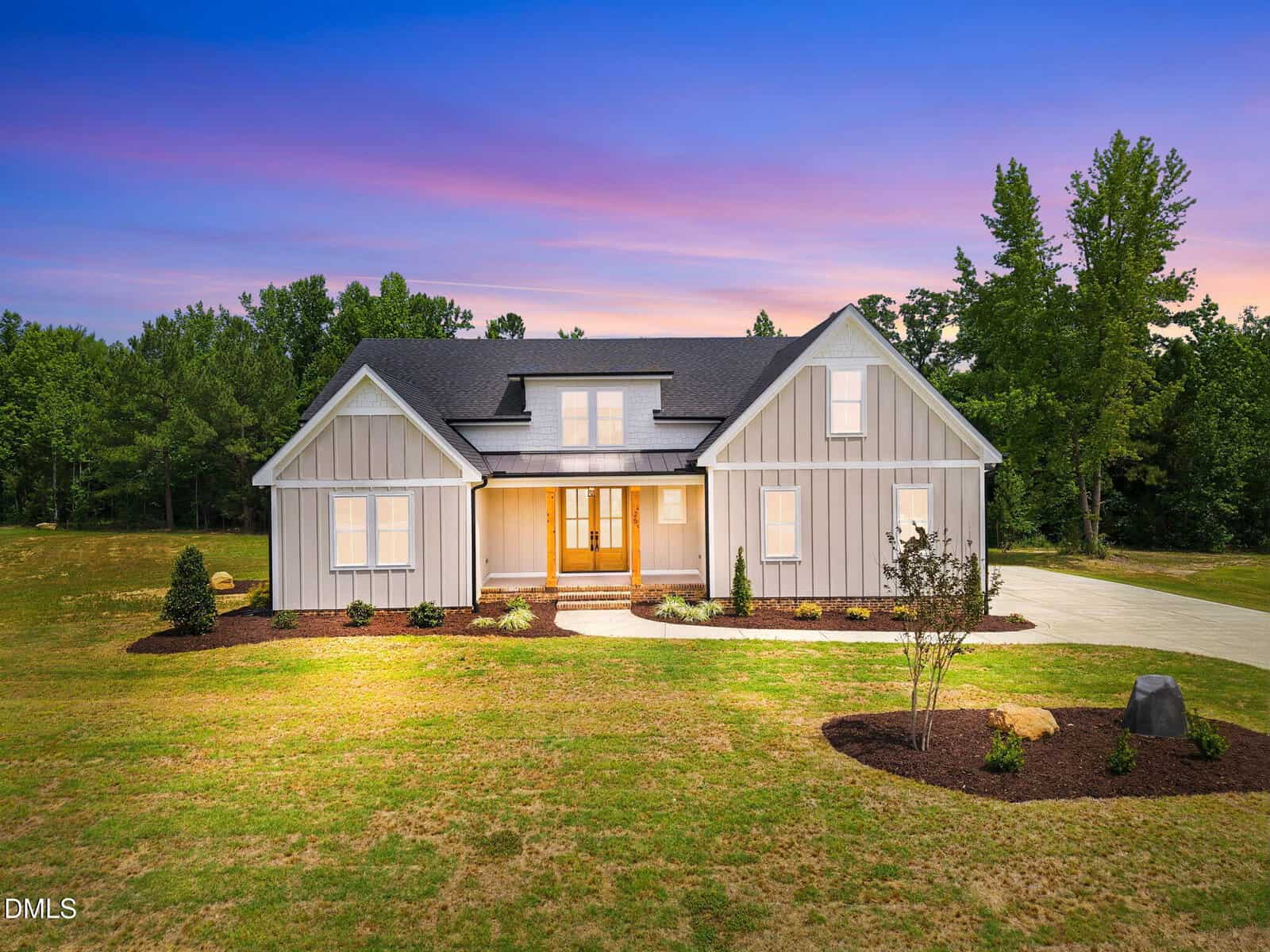 Modern farmhouse-style home at 25 Serenity Woods Trail in Franklinton, featuring white board and batten siding, black roof, large windows, and a front porch set against a vibrant sunset sky with trees and landscaped yard.