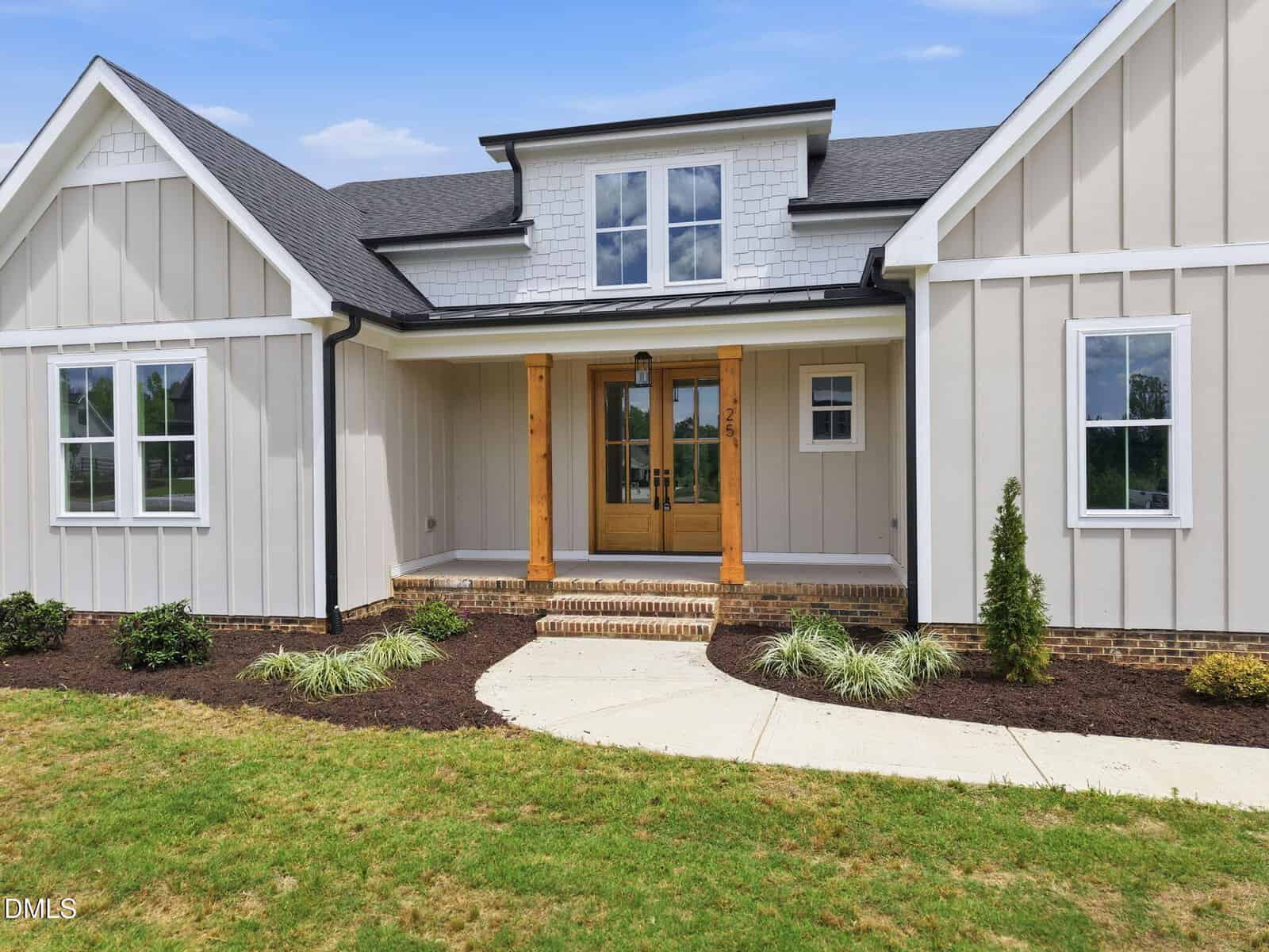 Single-story modern farmhouse with board and batten siding, double wooden front doors with glass panels, a small covered porch with brick steps, and landscaped front yard with shrubs and mulch.
