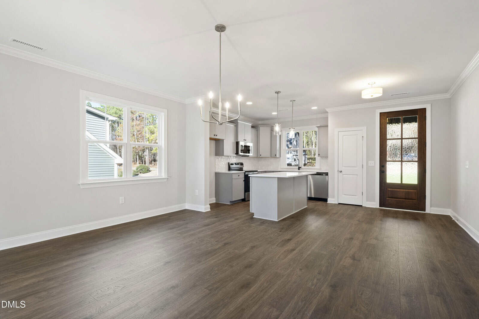 Modern open-concept kitchen and dining area with hardwood floors, white walls, large windows, island with bar stools, stainless steel appliances, and a wooden front door.