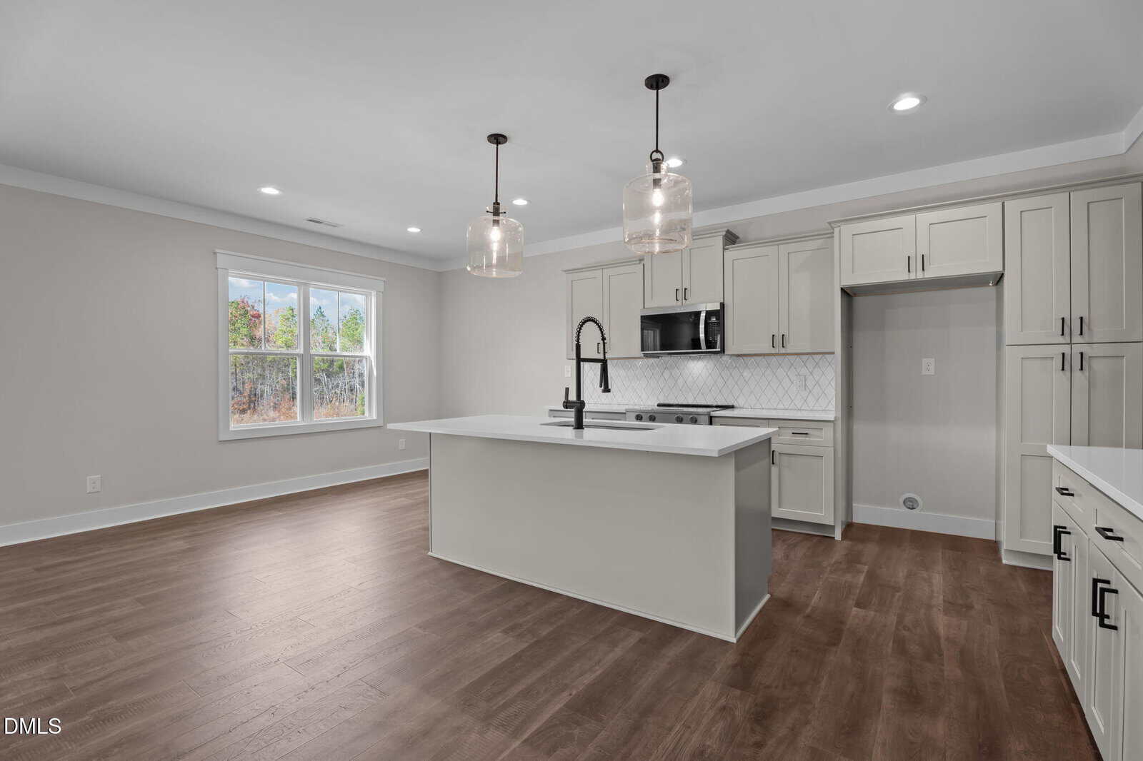 Modern kitchen with light-colored cabinets, a white island, stainless steel appliances, pendant lights, wood flooring, and a large window letting in natural light. The space is open and freshly finished.