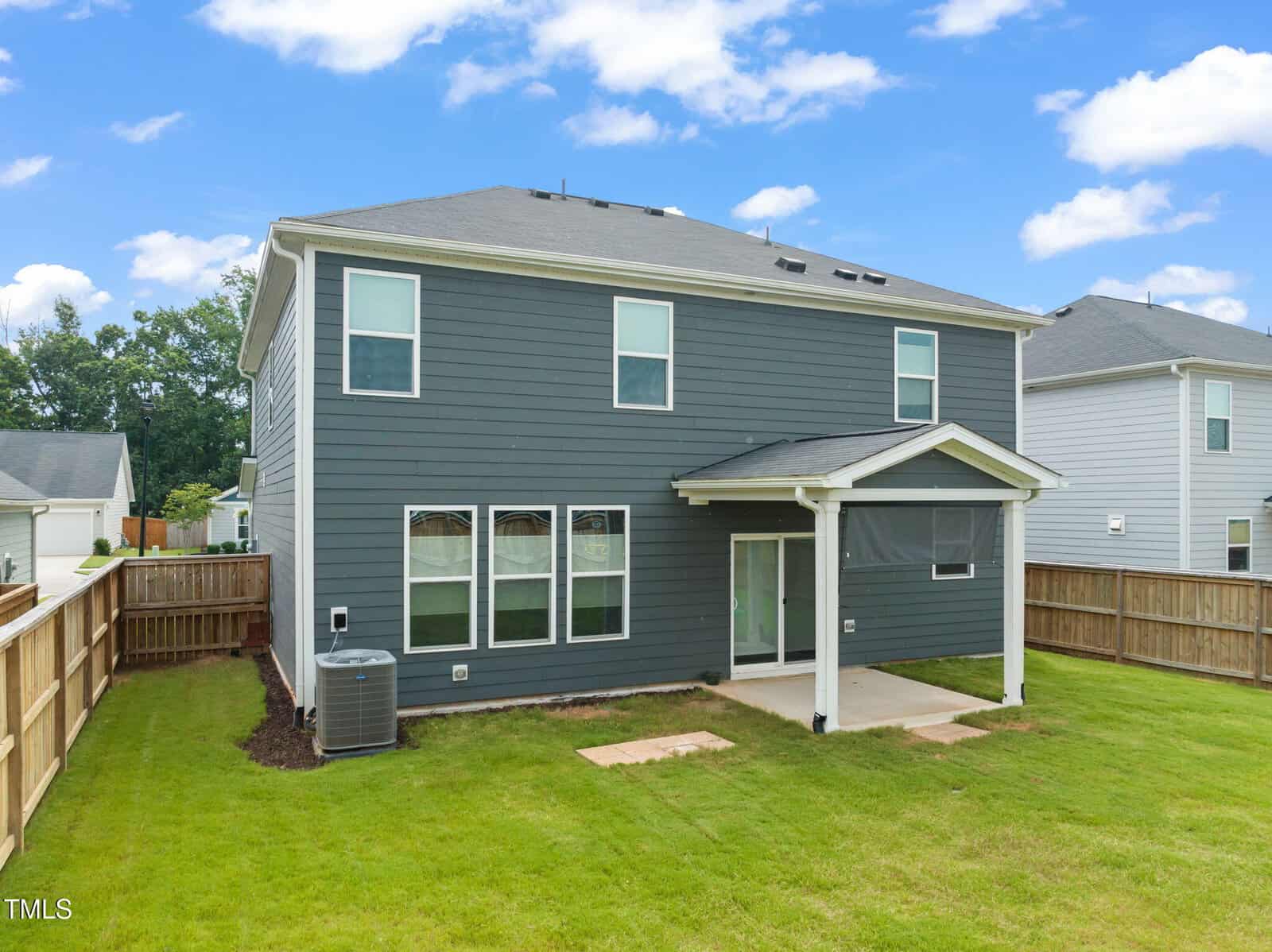 A two-story gray house with white trim, a covered patio, fenced backyard, and green grass under a partly cloudy blue sky.