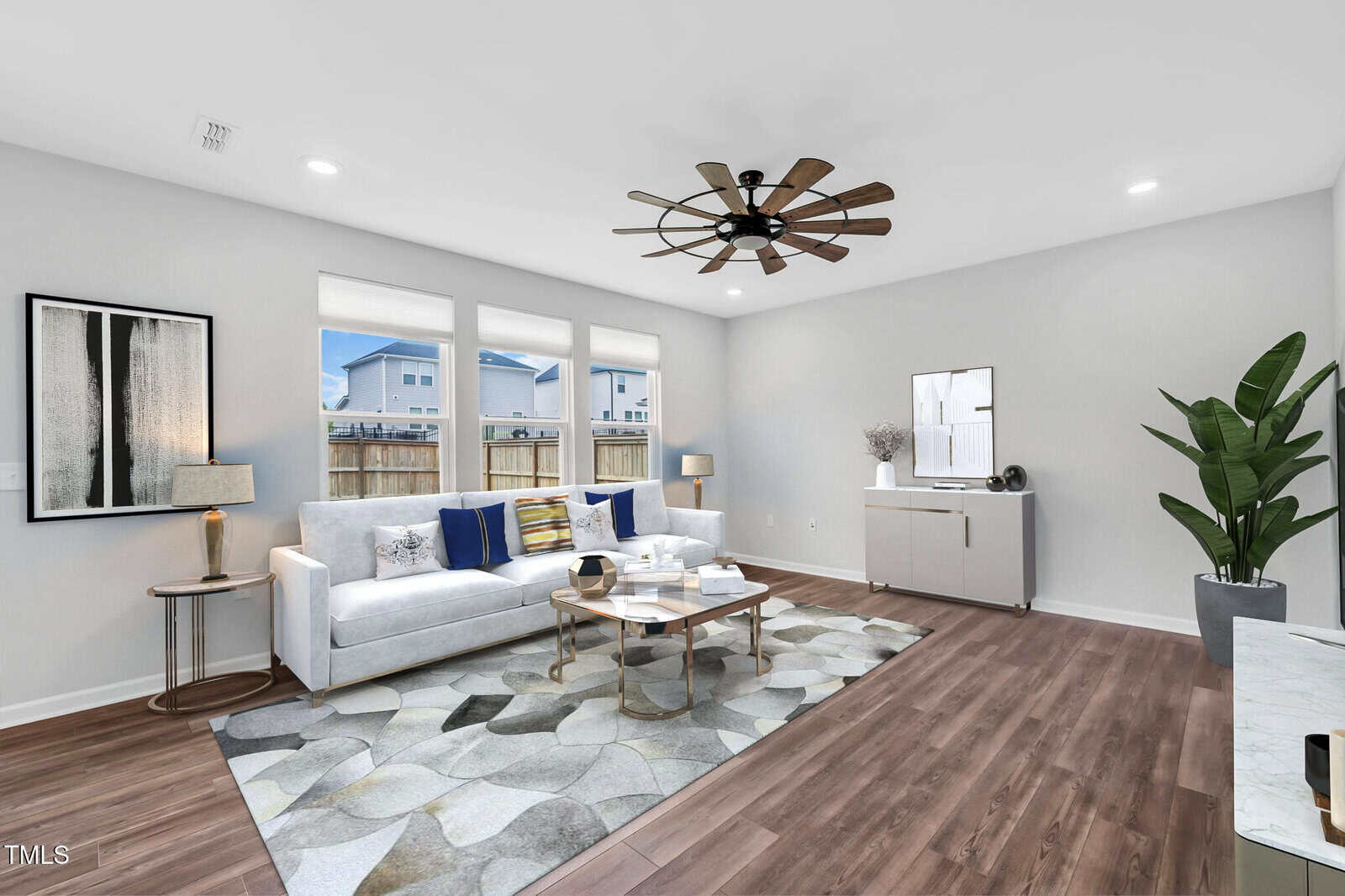 A modern living room with a white sofa, abstract rug, coffee tables, large ceiling fan, side tables with lamps, potted plant, credenza, and three tall windows letting in natural light.