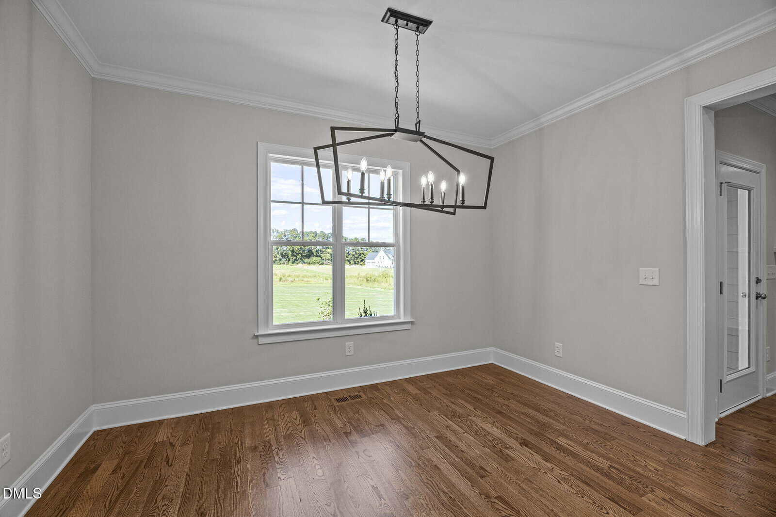 Empty dining room with light gray walls, wood floor, a large window showing greenery outside, and a modern rectangular chandelier hanging from the ceiling.