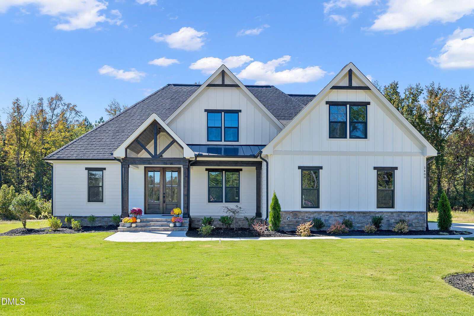 A modern farmhouse-style home at 1409 Cottondale Lane features white siding, dark trim, and a gabled roof. The front yard offers green grass, small shrubs, and a paved walkway leading to the entryway, with trees visible in the background.