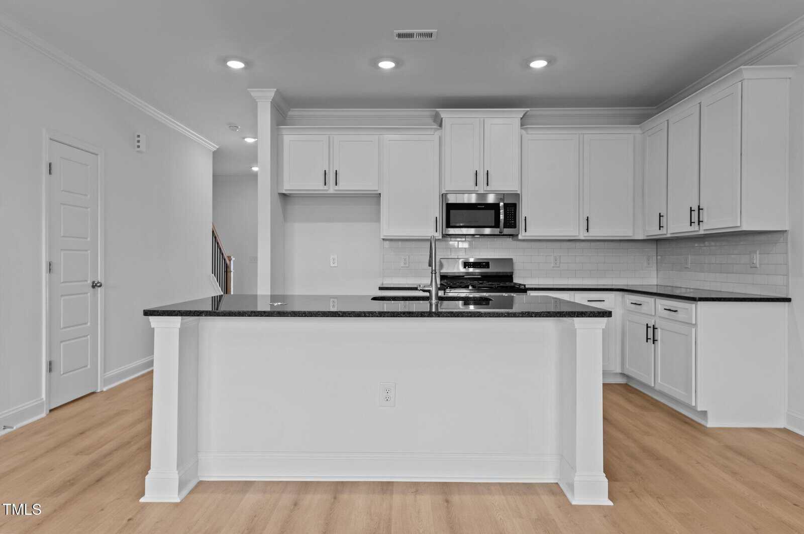 Modern kitchen with white cabinets, stainless steel appliances, a black granite island countertop, subway tile backsplash, and light wood flooring. Recessed ceiling lights illuminate the space.