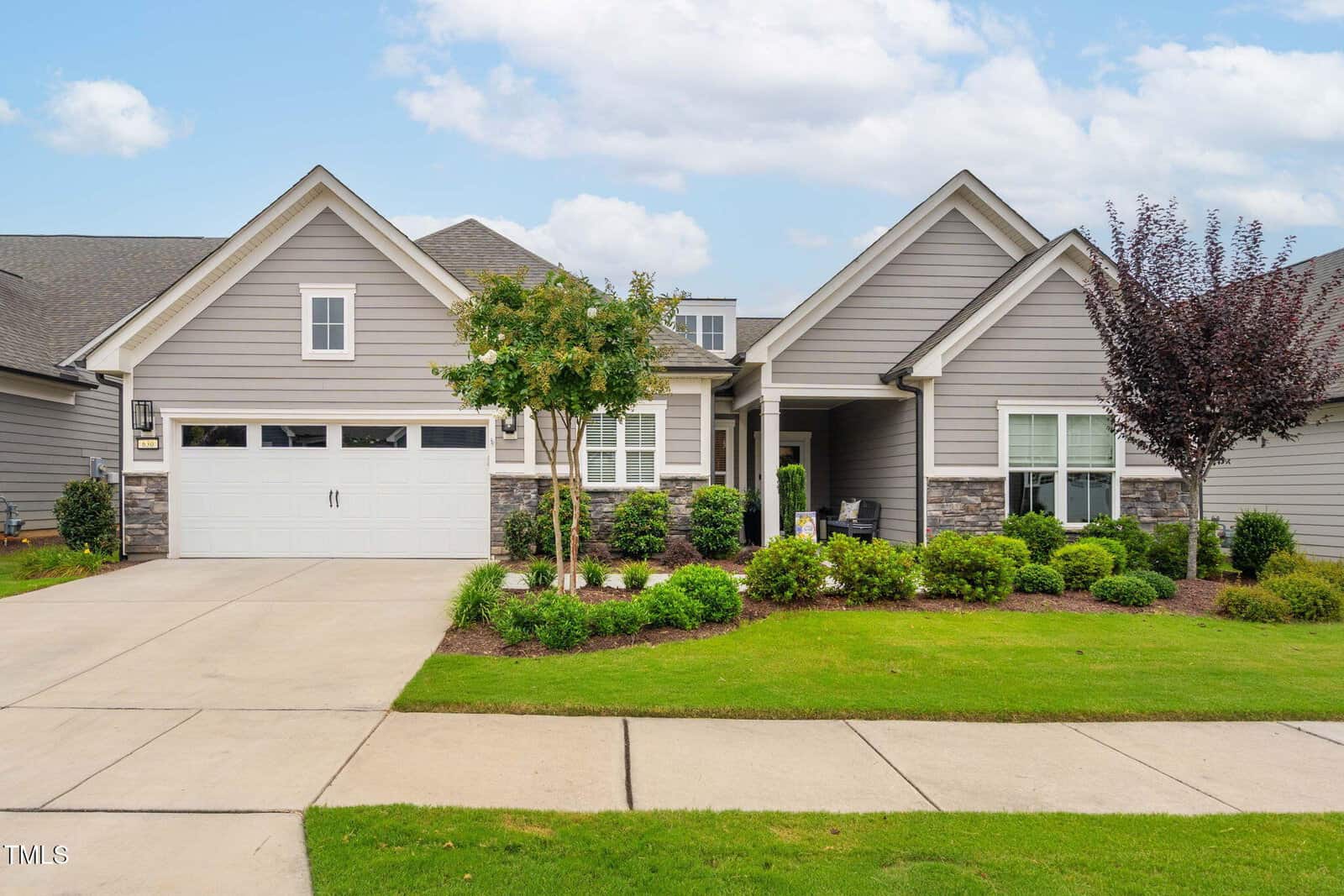 Charming single-story gray house with white trim, stone accents, and a two-car garage located at 630 Carneros Street in Wake Forest. Enjoy a well-maintained lawn, manicured shrubs, and a small tree in front. Concrete driveway and sidewalk complete the inviting curb appeal under a partly cloudy sky.
