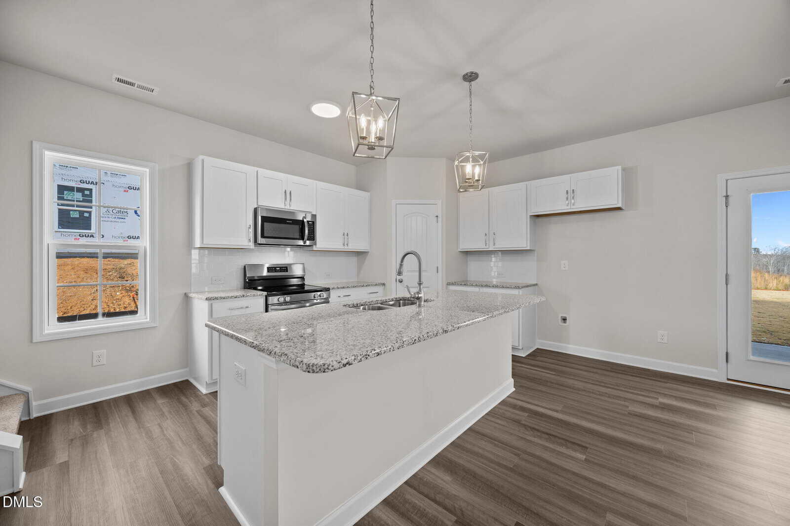 Modern kitchen with white cabinets, granite countertops, a center island with sink, stainless steel appliances, pendant lighting, wood flooring, and large windows letting in natural light.