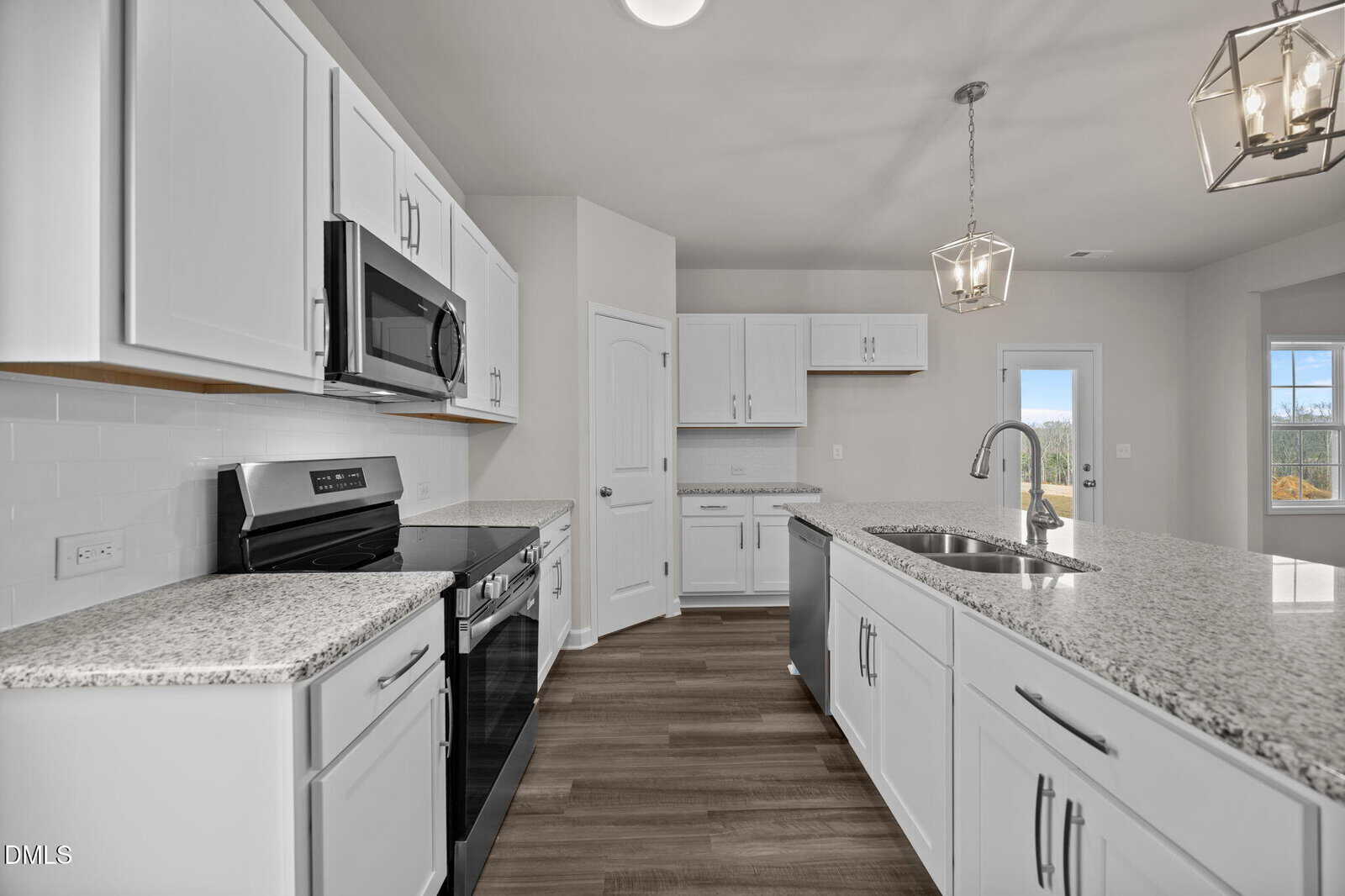 Modern kitchen with white cabinets, granite countertops, stainless steel appliances, a center island with a sink, pendant lighting, and wood flooring. Large windows in the background provide natural light.