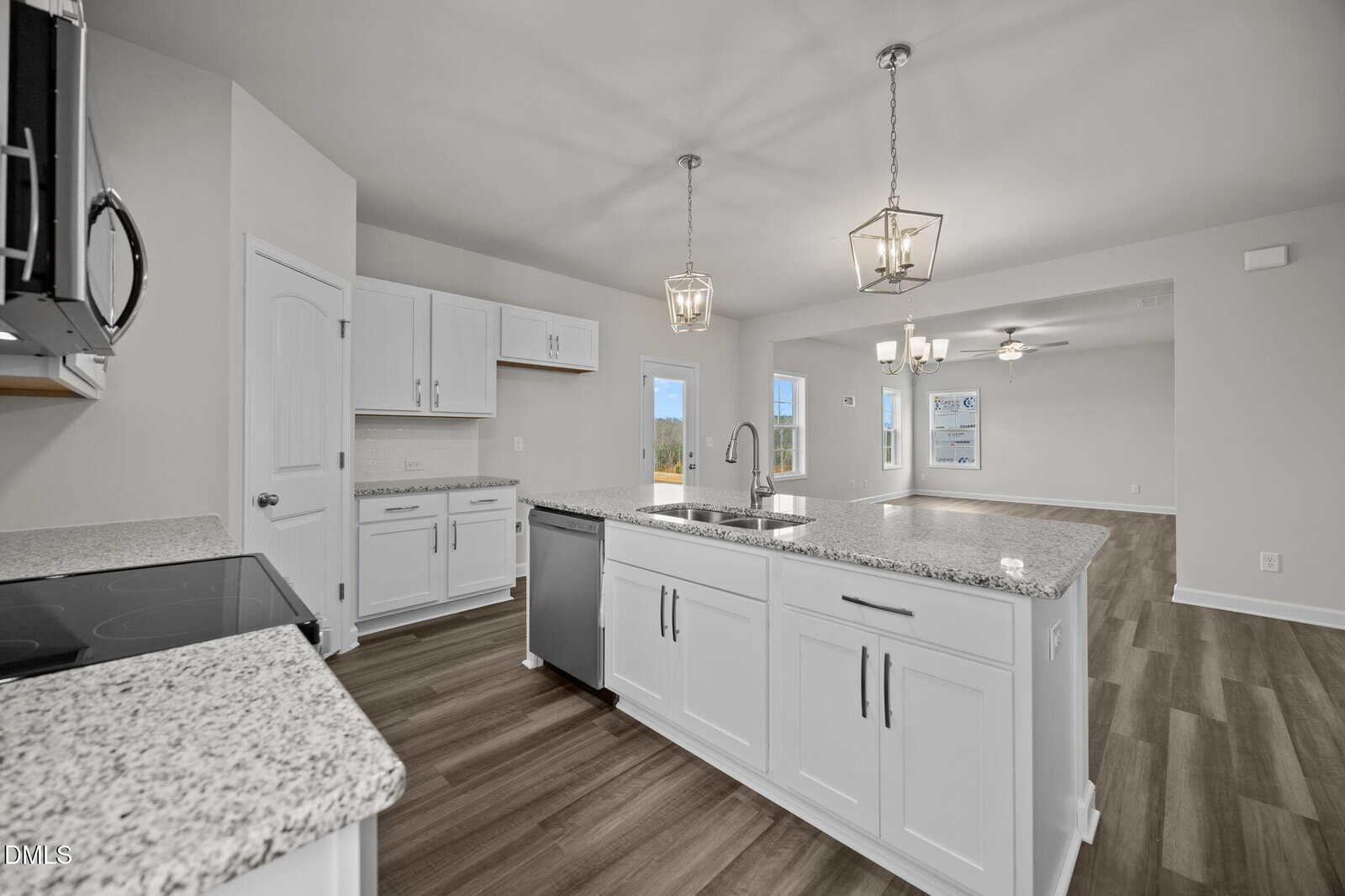 Modern kitchen with white cabinets, granite countertops, stainless steel appliances, center island with sink, and pendant lighting, opening into a spacious living area with wood-look flooring and large windows.