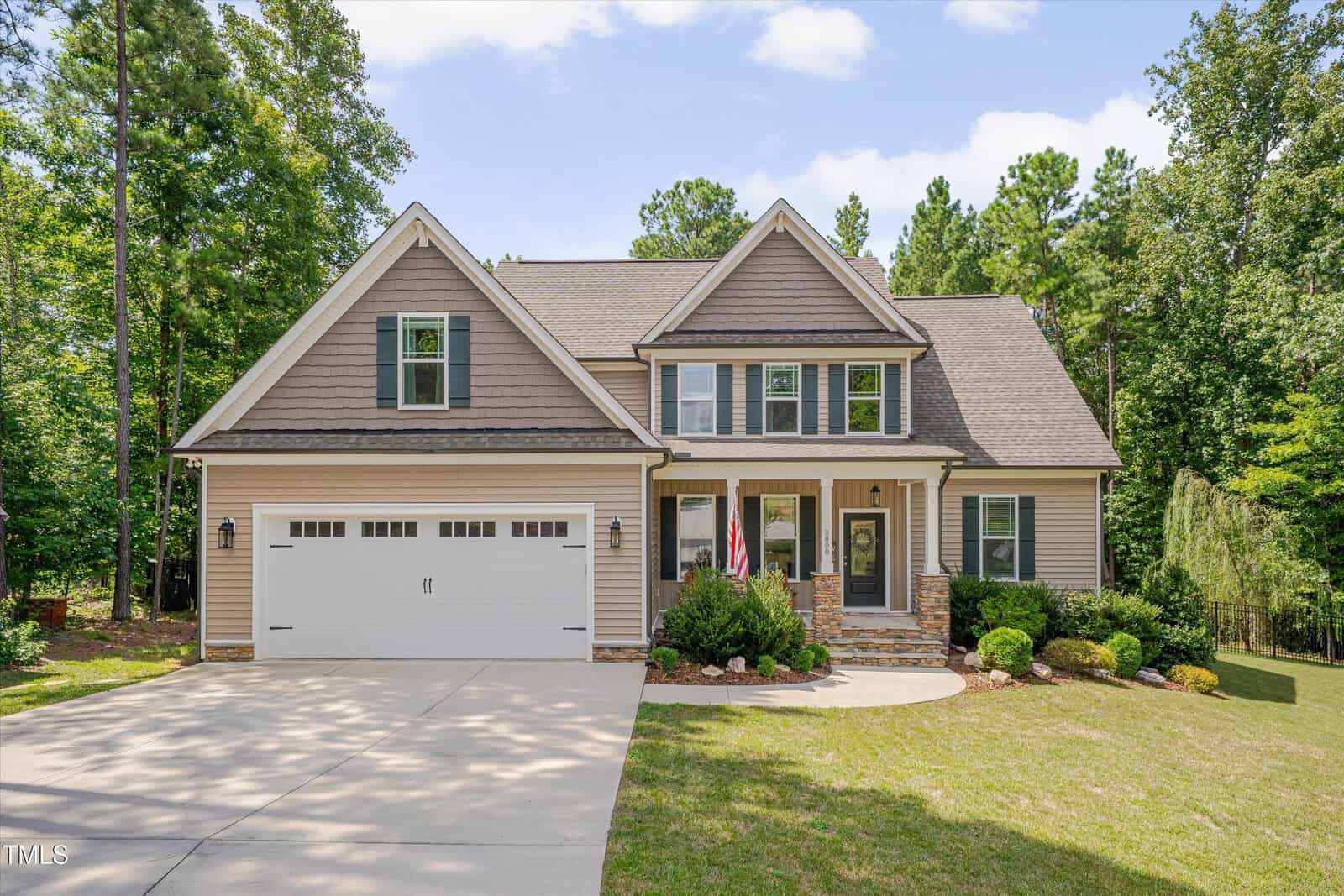 Located at 3800 Watermark Drive in Franklinton, this two-story suburban house features beige siding, stone accents, a front porch, and a two-car garage, nestled among green trees and landscaped shrubbery with an American flag by the entrance.