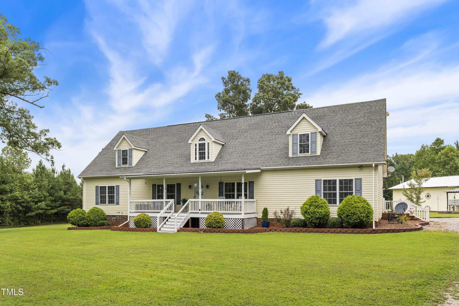 A large, light yellow house on 2150 NC 58 in Castalia features a front porch, dormer windows, and a well-kept lawn. Shrubs line the front while trees stand in the background under a partly cloudy sky.