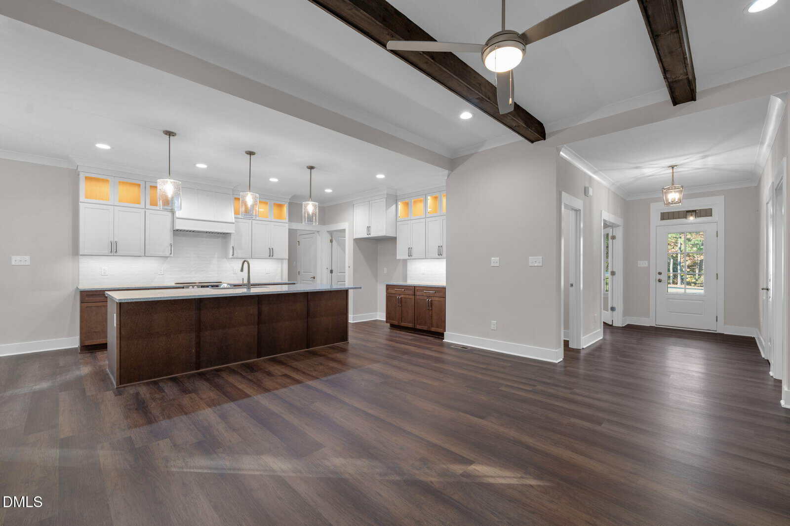 Spacious modern kitchen and living area with dark wood floors, white cabinets, exposed ceiling beams, pendant lights, and large windows near the entrance door.