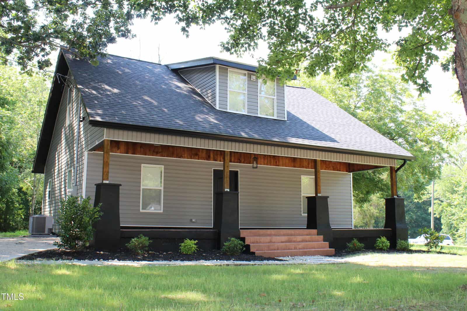A gray house with a black roof at 405 Sycamore Street in Oxford features a covered front porch with wood accents, black columns, and brown steps, surrounded by grass, small shrubs, and trees in the background.