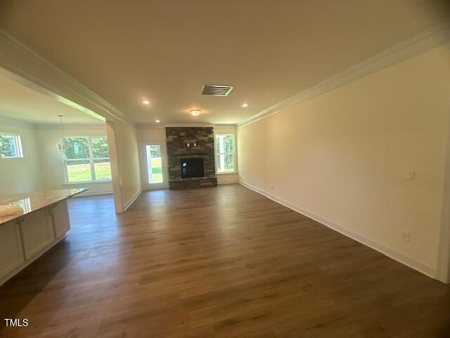Spacious living room with light wood flooring, white walls, and recessed lighting. A stone fireplace is centered on the far wall, with large windows on either side letting in natural light. An open kitchen area is to the left.