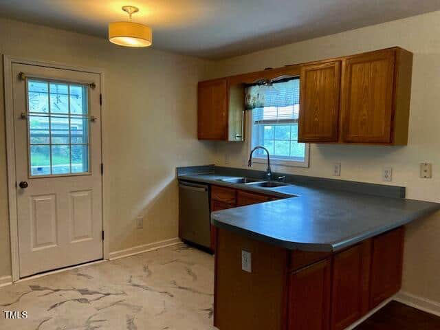 Kitchen with wood cabinets, gray countertops, stainless steel appliances, a double sink, a window with blinds, tiled floor, and a white door with a window leading outside. Ceiling light fixture above.