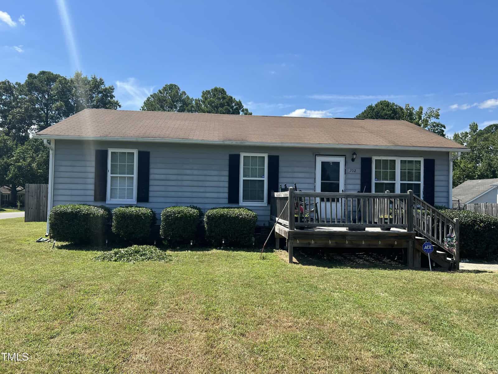Single-story house at 202 Peachtree Street, Creedmoor, with light gray siding, dark shutters, and a brown shingle roof. A wooden ramp and small porch greet you at the entrance, with neatly trimmed bushes lining the front.