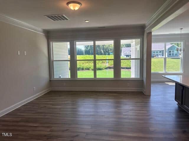 A bright, empty living room with wood floors, large windows overlooking a green yard, and an adjacent dining area. White walls and ceiling with crown molding, letting in plenty of natural light.