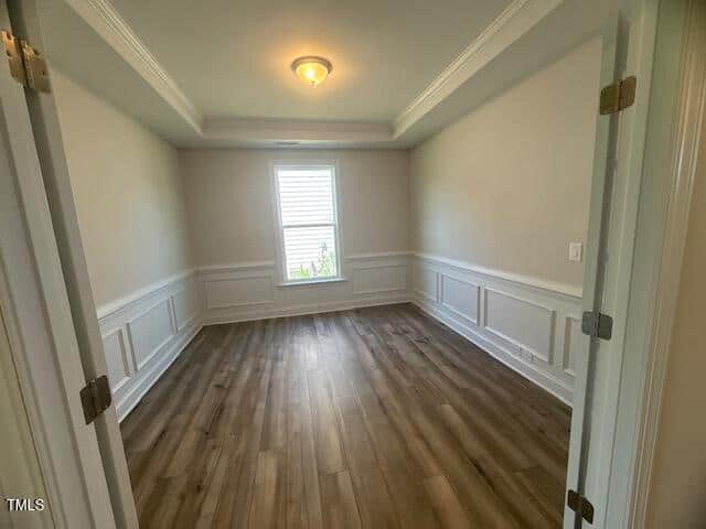 A bright, empty room with light-colored walls, wood flooring, white trim and wainscoting, a large window at the far end, and a ceiling light fixture. Double doors open into the space.