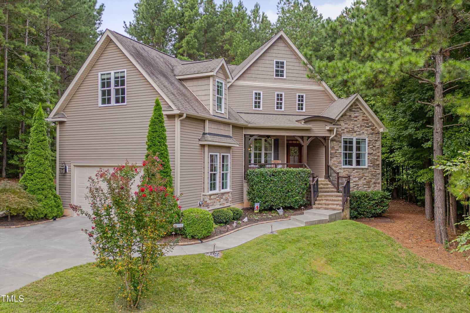 Charming two-story house at 1633 Carriage Drive, Franklinton, with beige siding and stone accents. Surrounded by trees and shrubs, it features a covered porch with railing and well-maintained landscaping.