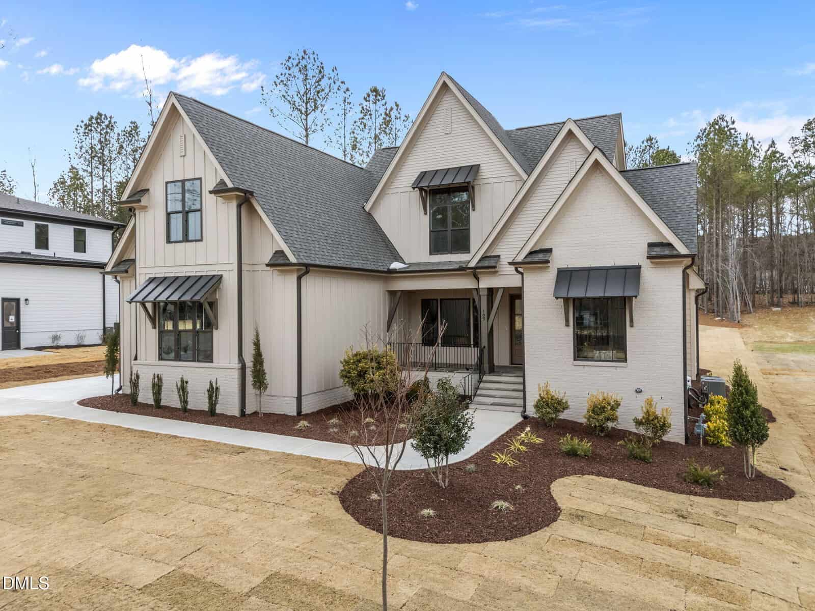 A modern two-story house with light-colored siding, black trim, and a covered front porch; black metal awnings over several windows and newly landscaped front yard with young shrubs and trees.