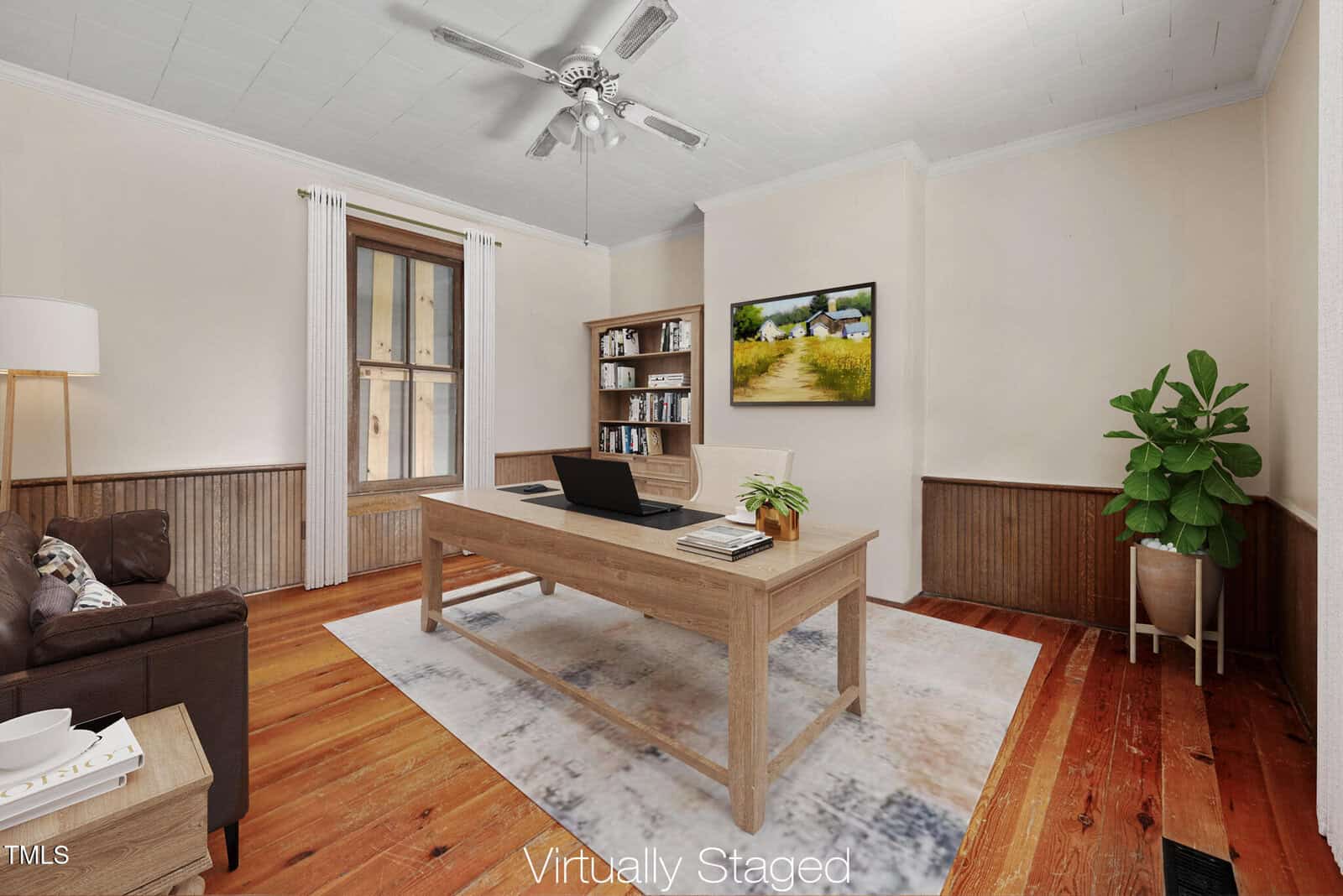 A home office with wood floors, beige walls, a wooden desk, a laptop, a brown leather couch, a bookshelf, a potted plant, and a window. "Virtually Staged" text appears at the bottom of the image.