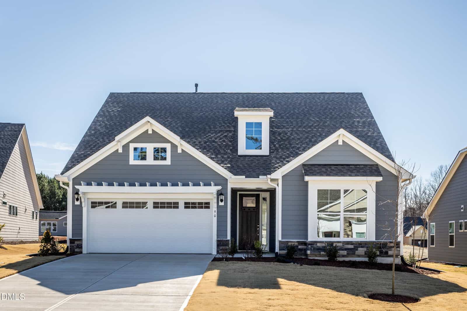 A modern, gray two-story house with white trim at 90 Slippery Elm Road in Youngsville features a front porch, large windows, a double garage, and a neatly manicured lawn under a clear blue sky.