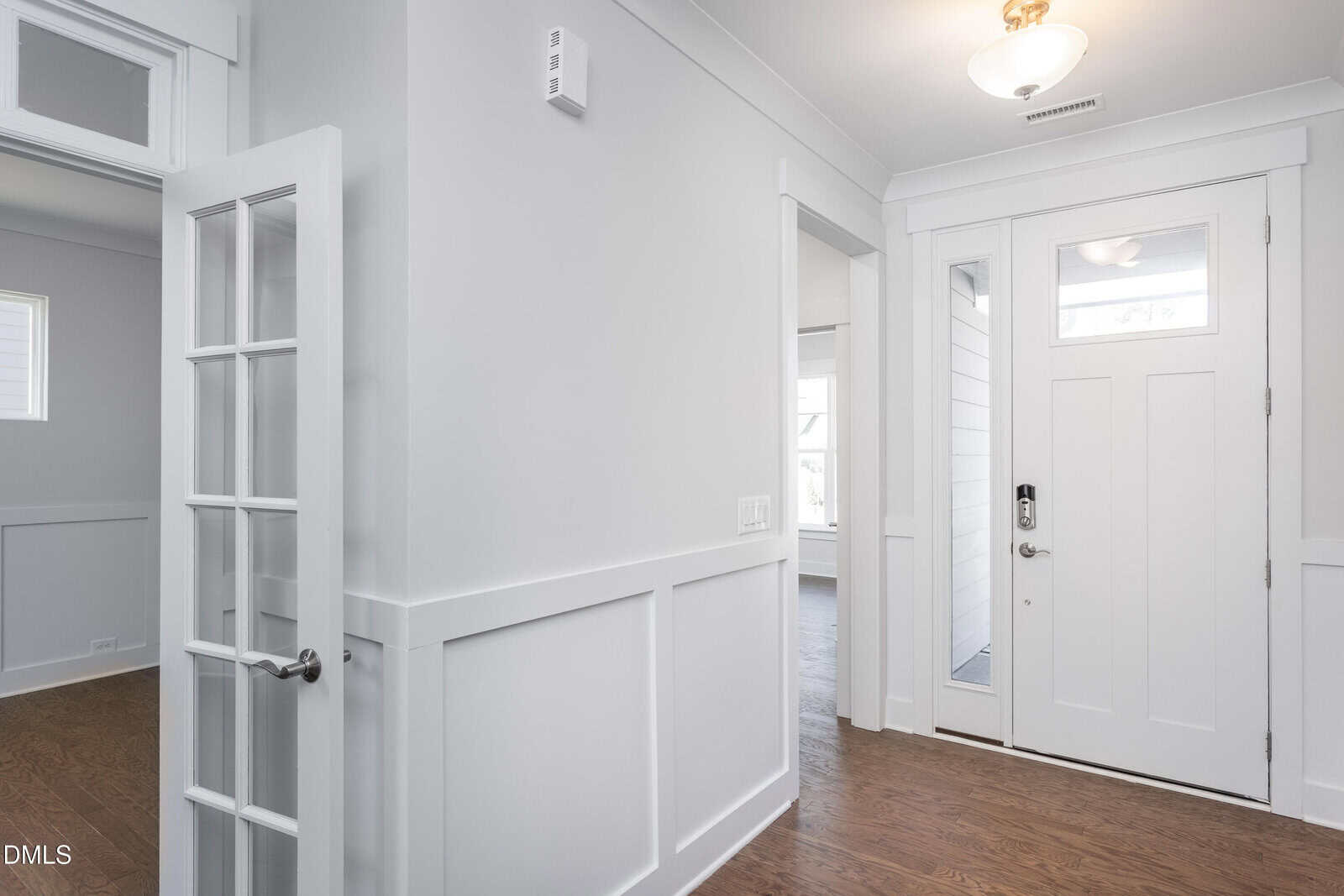 Bright entryway of a modern home with white walls, wood floors, a front door with glass panels, a side window, a ceiling light, and a French door leading to another room.