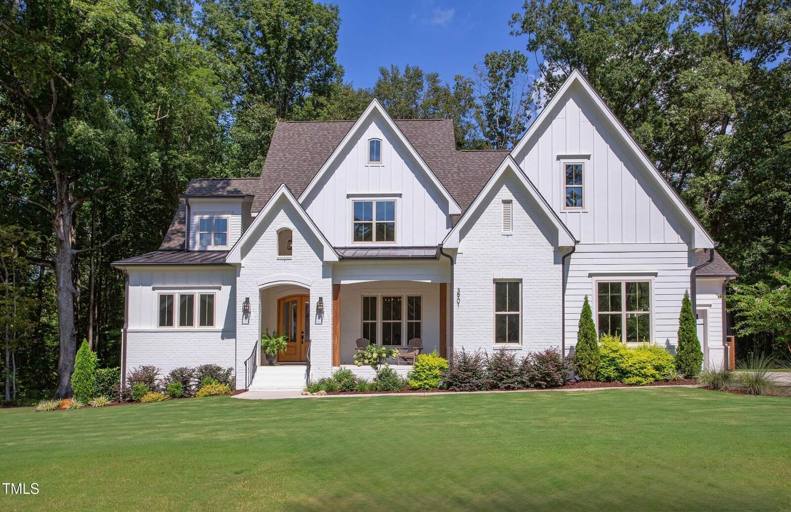 A large modern white house with a gabled roof at 3901 Laurel Creek Lane, Wake Forest, featuring a front porch and well-maintained lawn, surrounded by trees and landscaped shrubs on a sunny day.