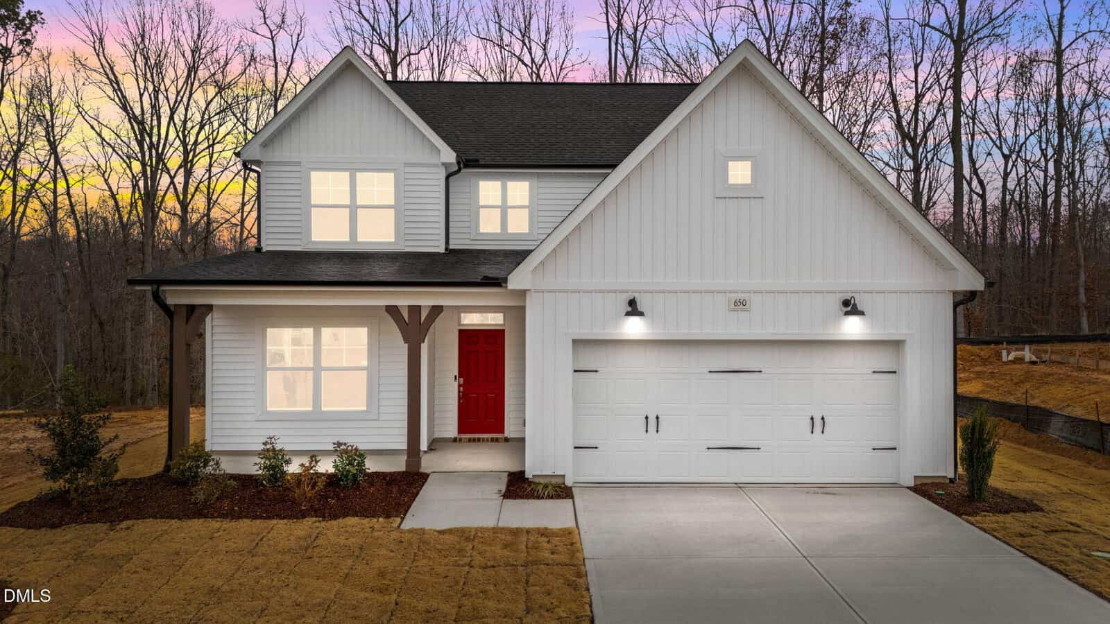 A modern two-story white house at 650 Husketh Road, Youngsville, featuring a red front door, double garage, and outdoor lights. The newly landscaped yard is framed by leafless trees in the background at sunset.