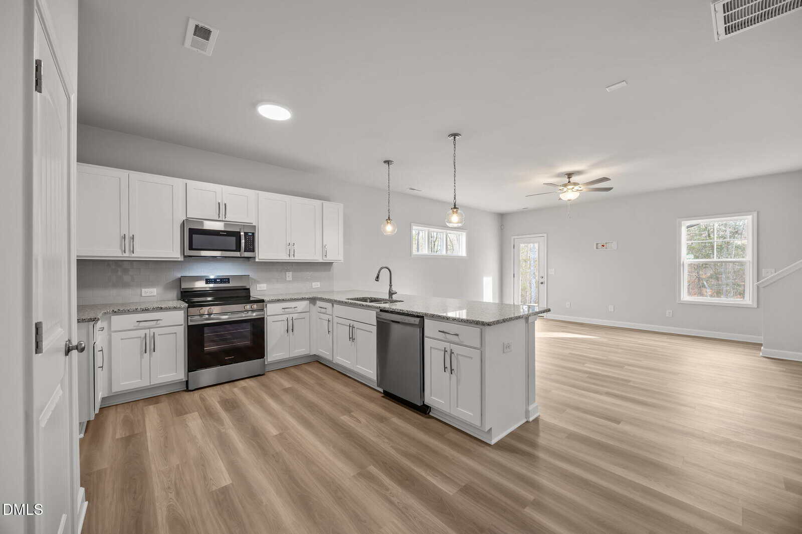 Modern open-concept kitchen and living area with light wood floors, white cabinets, stainless steel appliances, granite countertops, pendant lights, and large windows letting in natural light.