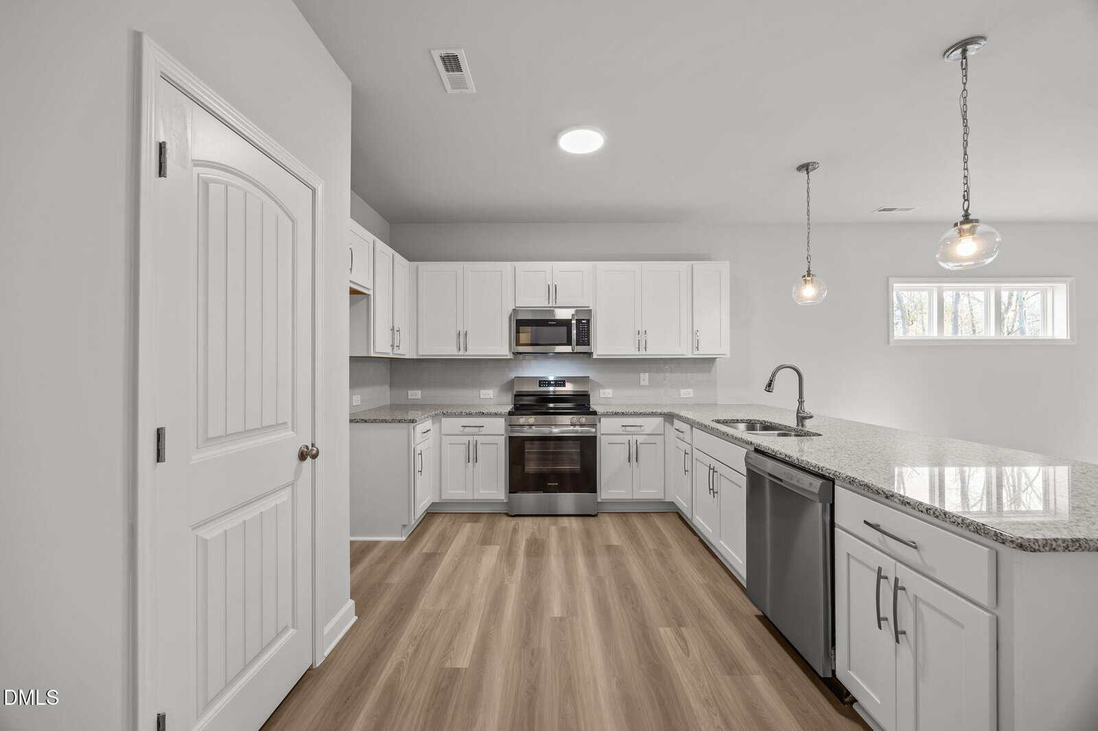 Modern kitchen with white cabinets, stainless steel appliances, granite countertops, two pendant lights over a large island, wood-style flooring, and a window providing natural light.