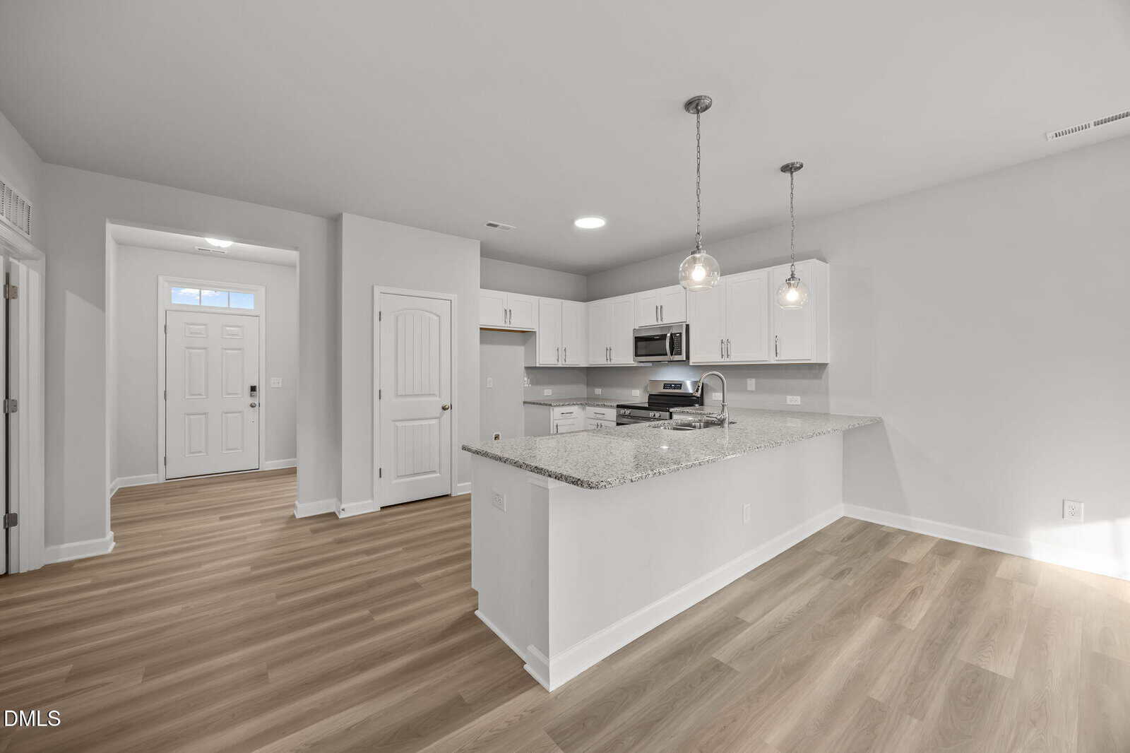 Modern kitchen with white cabinets, granite countertops, stainless steel appliances, pendant lights, and wood flooring. Entryway with door and closet is visible to the left. Room is bright with neutral colors.