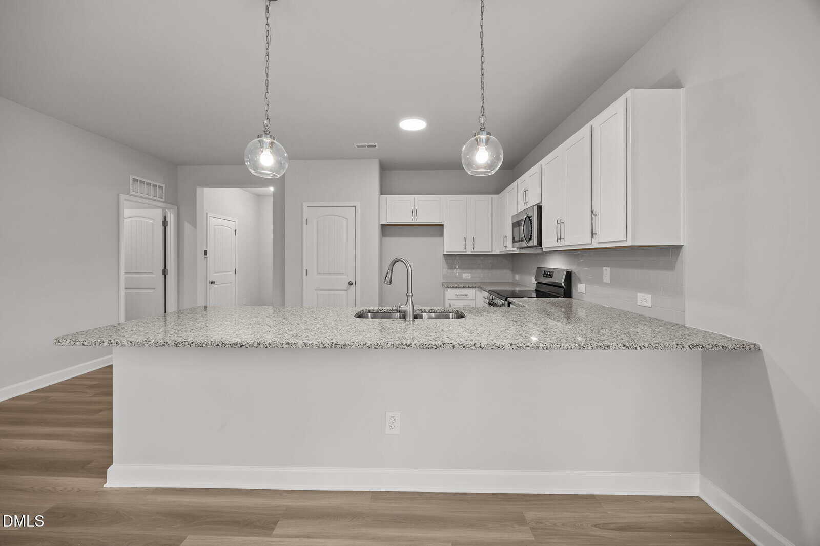 Modern kitchen with granite countertops, white cabinets, stainless steel appliances, two hanging pendant lights, and wood flooring. The space is clean, spacious, and open, with a neutral color scheme.