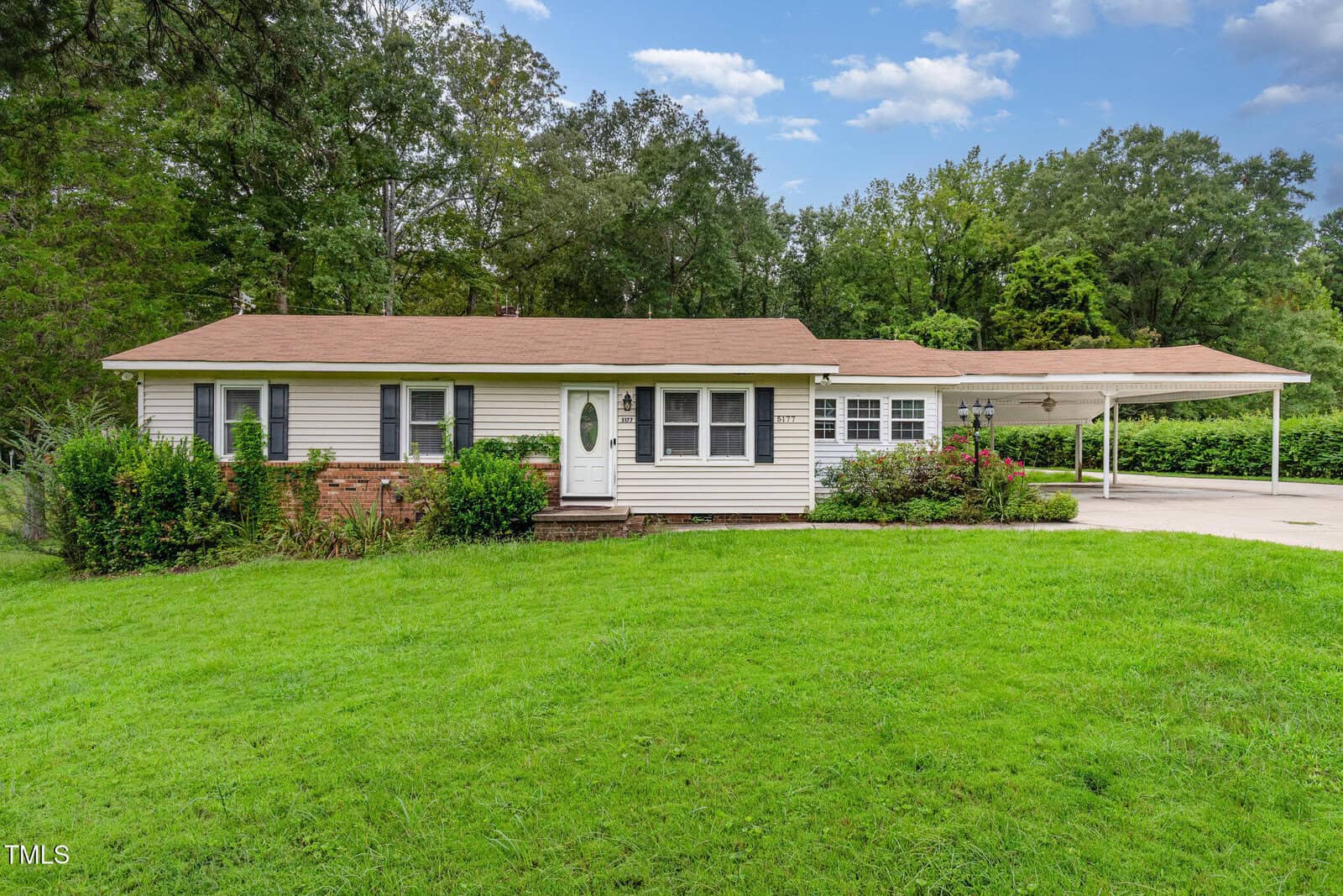 Charming single-story Oxford home at 5177 Forest View Height Road with light-colored siding, brick accents, and a brown shingle roof. Features a cozy porch, several windows, carport on the right, and is surrounded by green grass and trees.