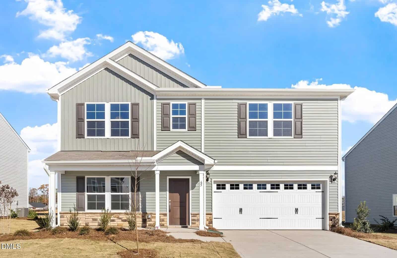 Charming two-story suburban house at 65 Plantation Drive, Youngsville, with light gray siding, stone accents, white trim, and a covered front porch. There are multiple windows and a double garage door. The front yard features sparse grass, young shrubs, and a concrete driveway.
