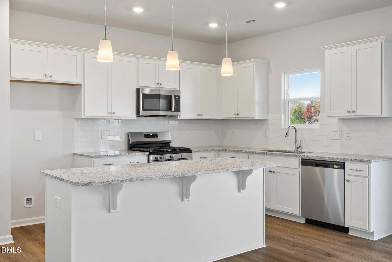 Modern kitchen with white cabinets, stainless steel appliances, granite countertops, subway tile backsplash, and pendant lights over a peninsula. There is a window above the sink and wood-style flooring.