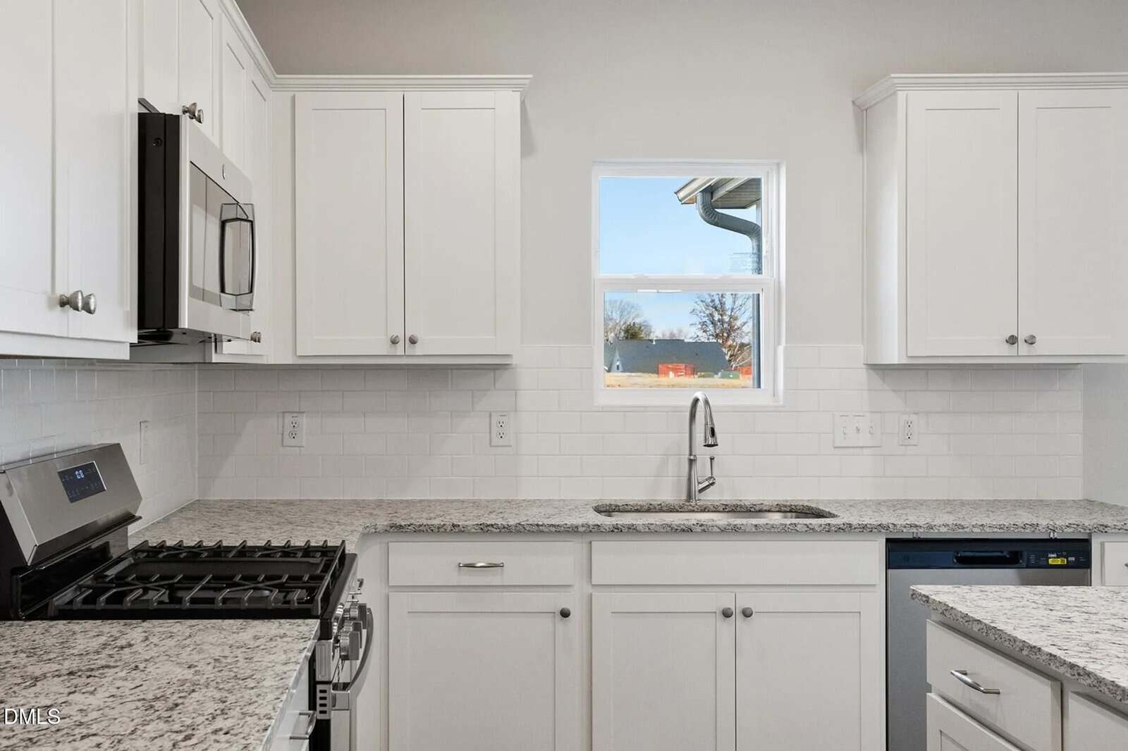 Modern kitchen with white cabinets, stainless steel appliances, a granite countertop, a single window above a sink, and a subway tile backsplash. The space appears clean and well-lit.