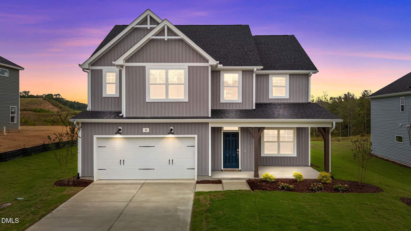 Charming two-story gray house with white trim at 30 Malbec Way, Youngsville. Features a double garage and covered porch, set against a vibrant sunset sky. Enjoy the well-maintained lawn and minimal landscaping out front.