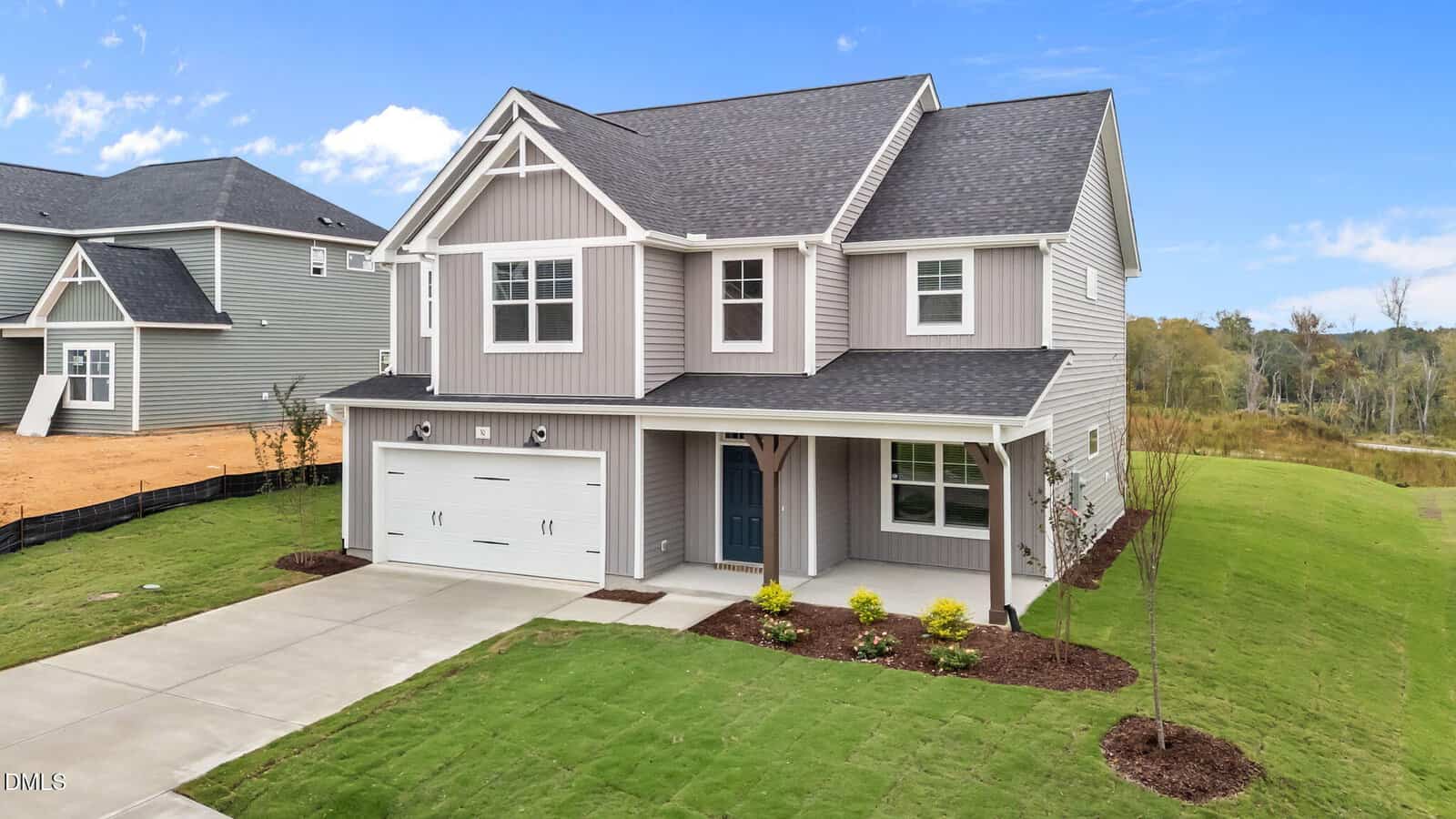A modern two-story gray house with white trim, a covered front porch, and a double garage sits on a freshly landscaped lawn under a blue sky.