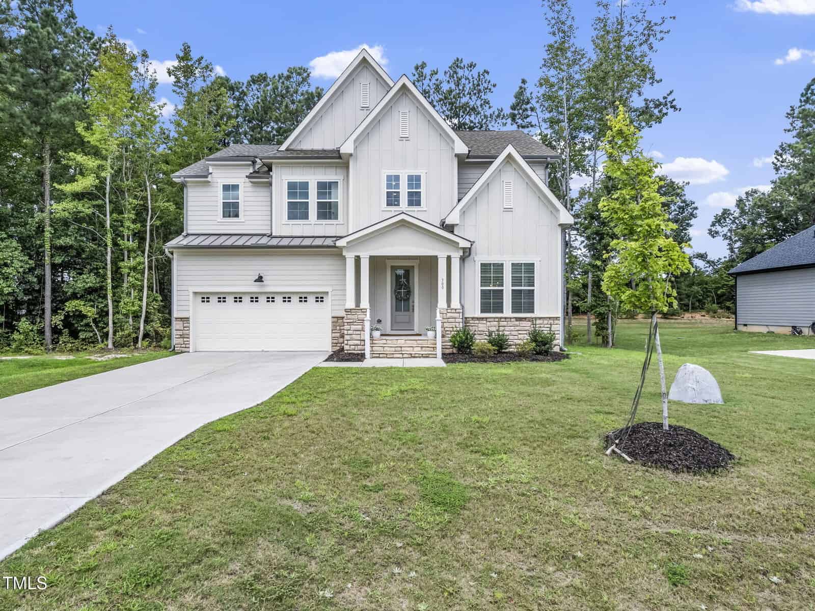 Two-story modern suburban house with light-colored siding, stone accents, and a covered front entry located at 300 Scotland Drive in Youngsville. There is a two-car garage, a concrete driveway, a small front yard, and trees in the background.
