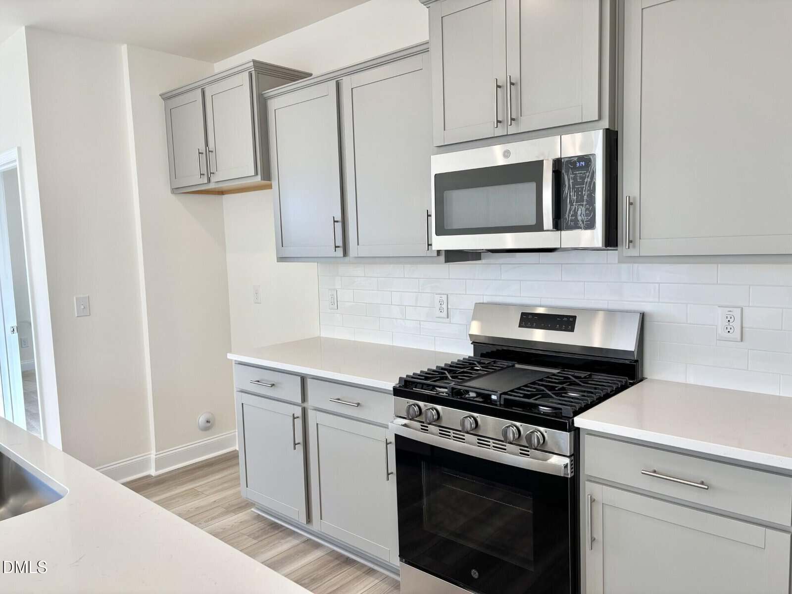 Modern kitchen with light gray cabinets, stainless steel gas stove and microwave, white subway tile backsplash, and light countertops. The room has neutral tones and a clean, minimalist design.