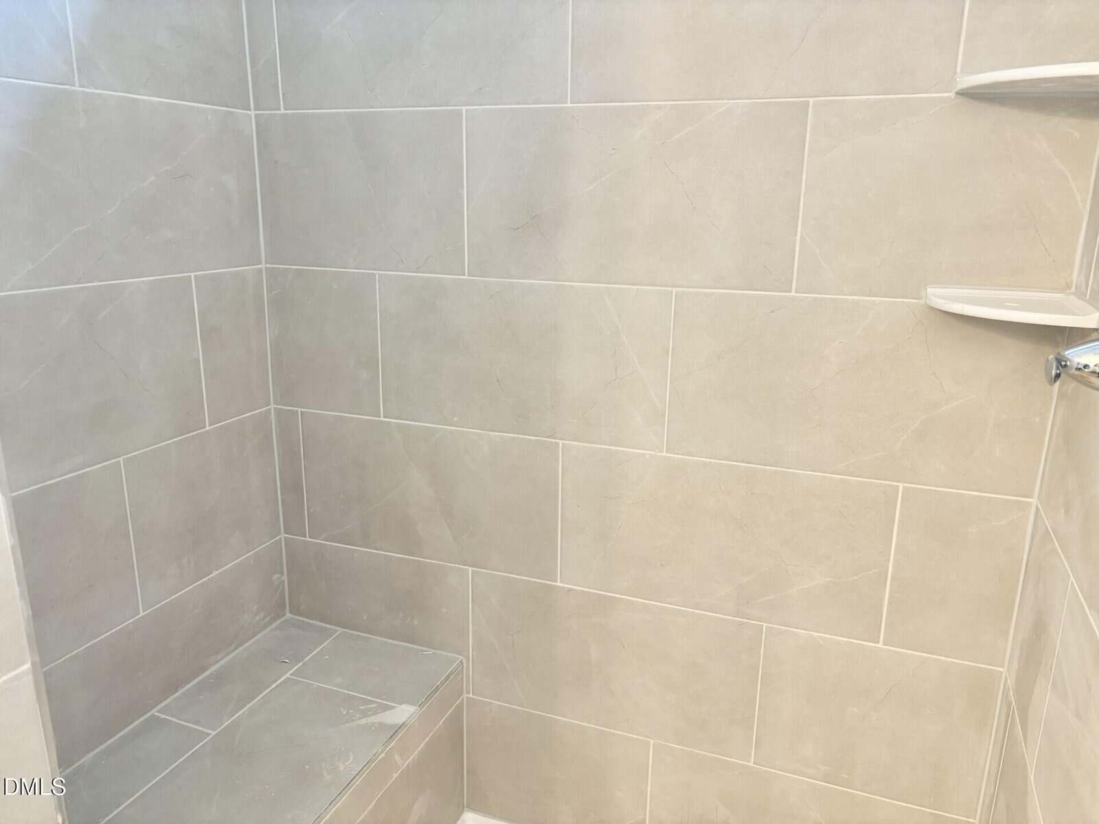 Shower with light gray tiles, a built-in bench, and two small corner shelves on the wall.