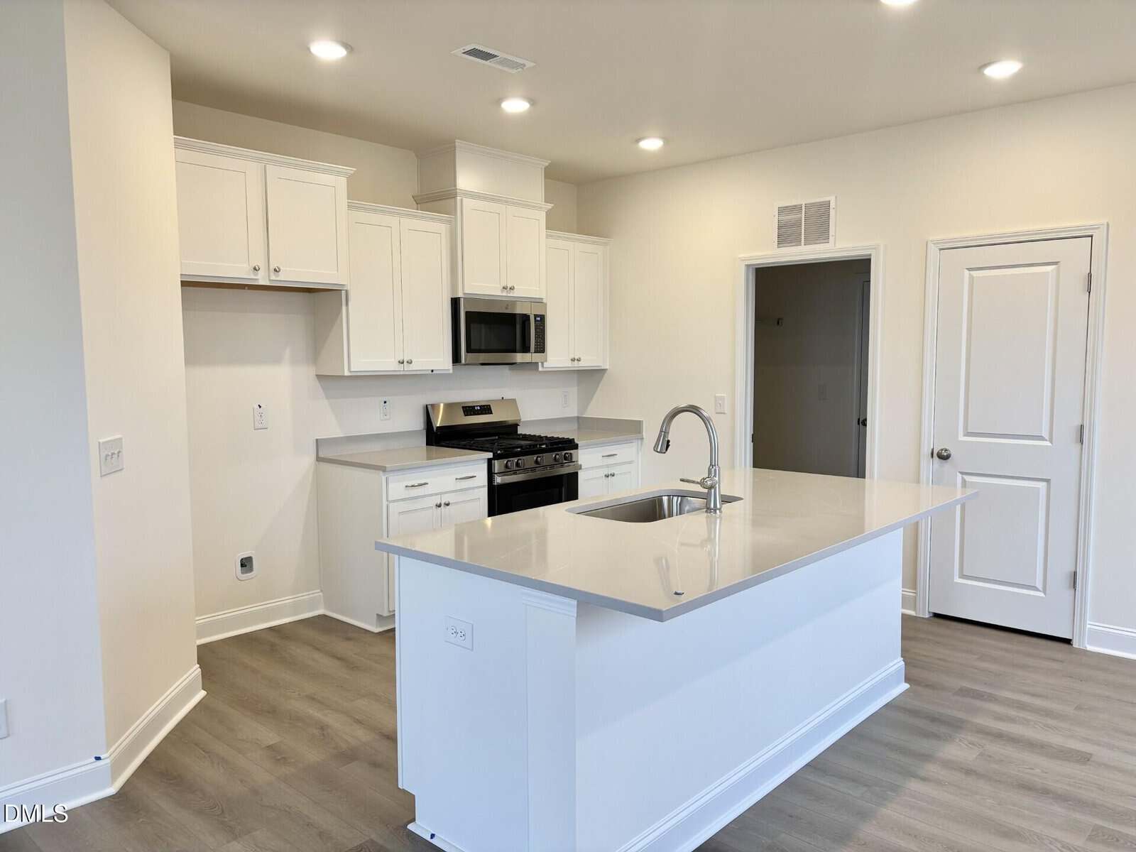 Modern kitchen with white cabinets, stainless steel appliances, a built-in microwave, gas stove, gray countertops, and a central island with a sink, all set on light wood flooring under recessed lighting.