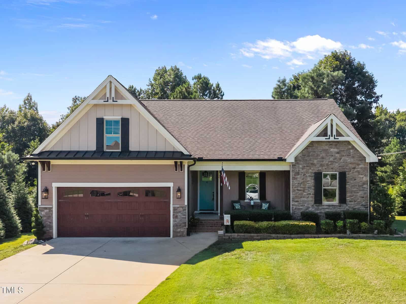 Located at 3658 Genesis Lane in Wake Forest, this charming one-story home features a gable roof, stone and siding exterior, two-car garage, inviting front porch with chairs, and a well-kept lawn. An American flag hangs near the porch amid shady trees.