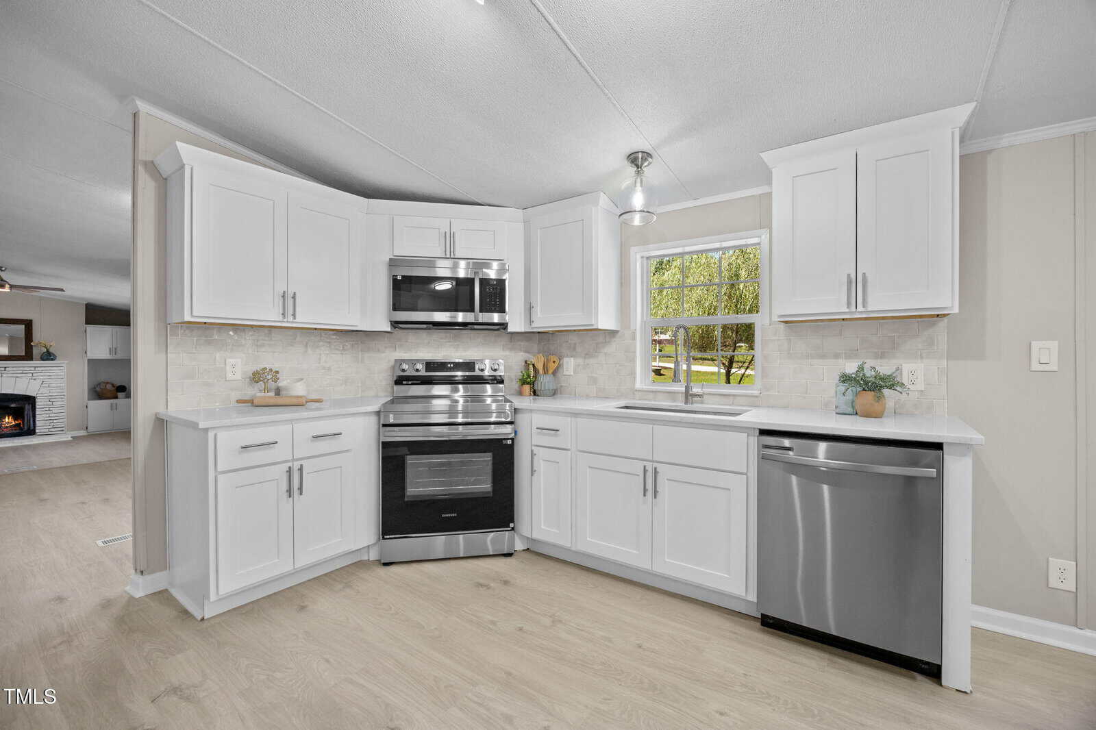 Modern kitchen with white cabinets, stainless steel appliances including a stove, oven, microwave, and dishwasher, light wood flooring, a window above the sink, and neutral-colored walls.